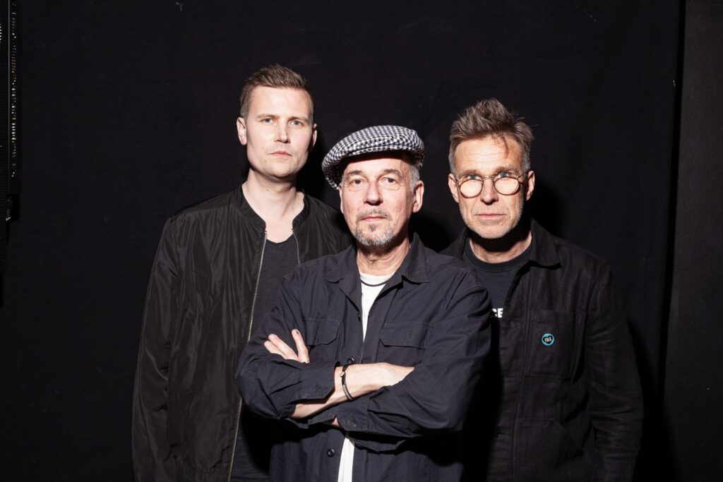 Musiktrion Les Brains: Jens Comén, Göran Månsson och Anders Åkered står framför en svart bakgrund, tittar rakt in i kameran. Anders bär keps, de andra har kort hår.
